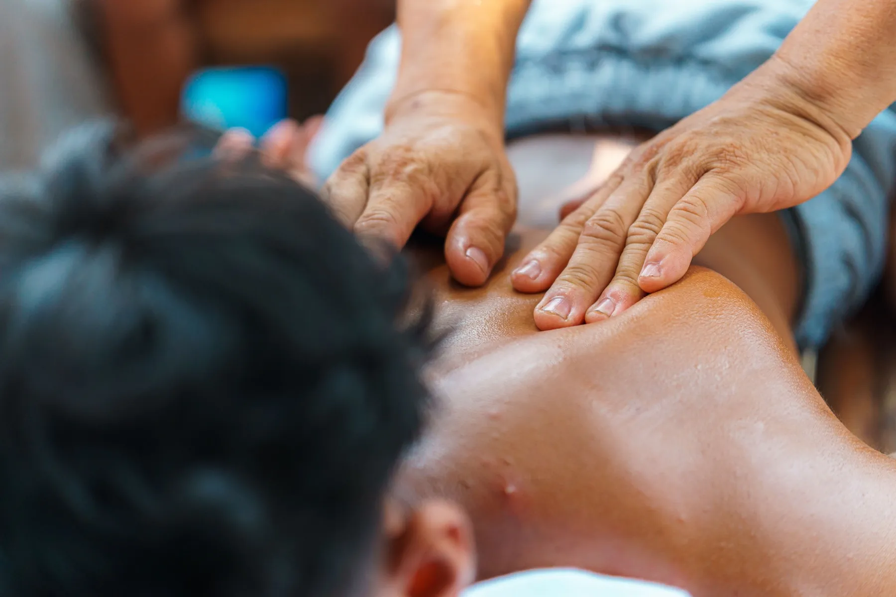 Therapist's hands working across a client's upper back and shoulders during a full body therapeutic massage