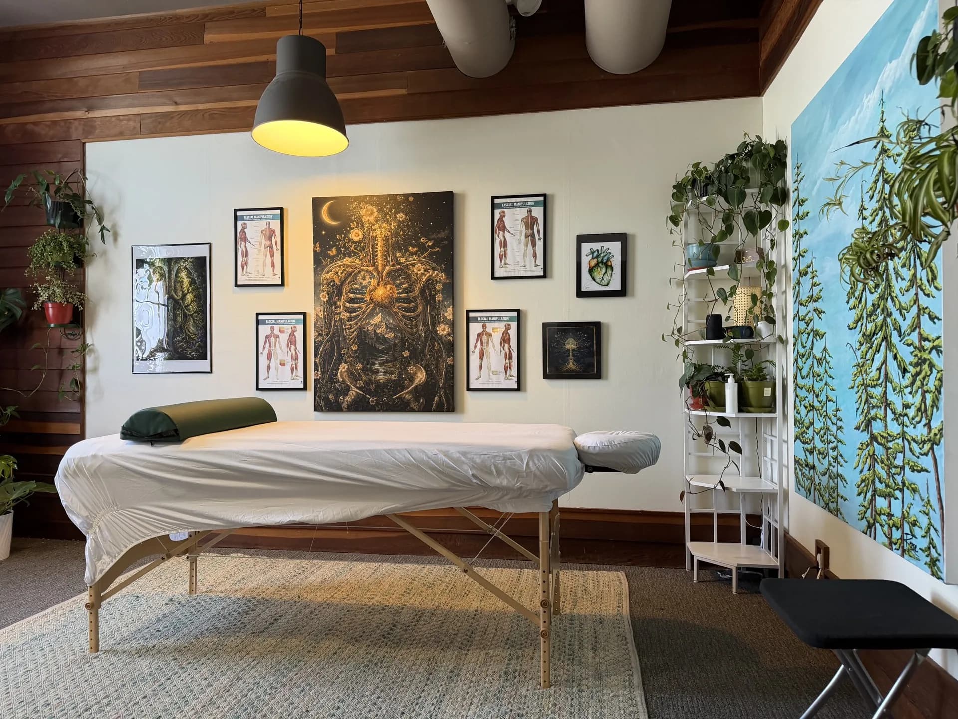 Treatment room in the Renewed Bodyworks Eugene studio with massage table, anatomy art wall, and pine mural