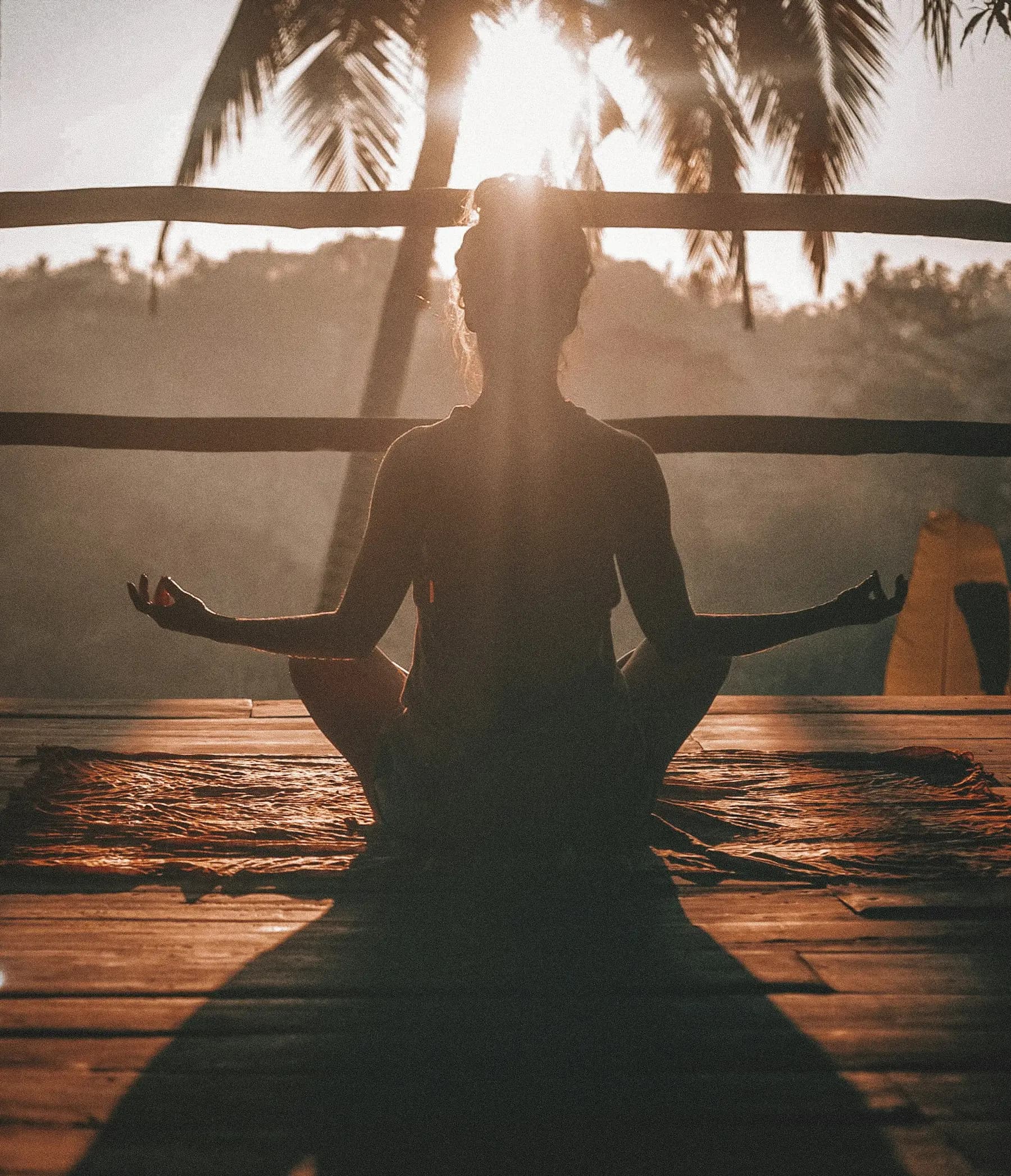 Person meditating at sunrise, framed by warm morning light